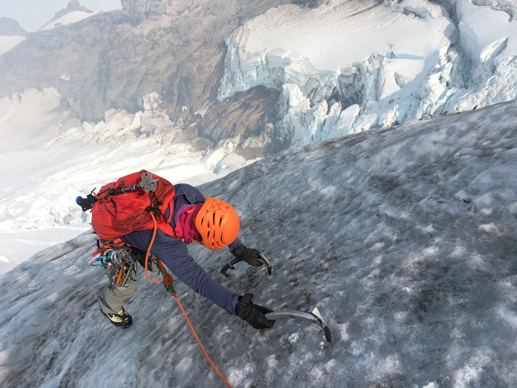Woman mountaineer testing boots on snowy peak with ice axe and crampons