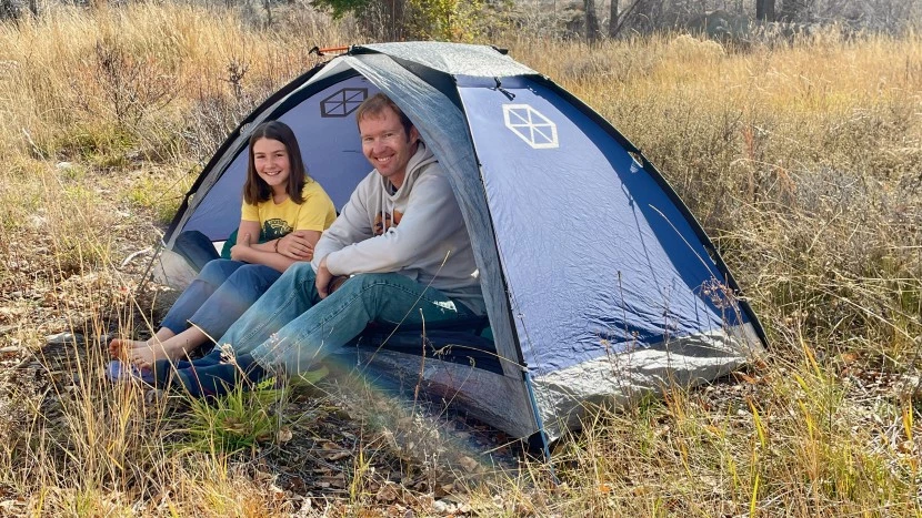 Forest camping tent setup with proper guy lines and weather protection in dense woodland environment